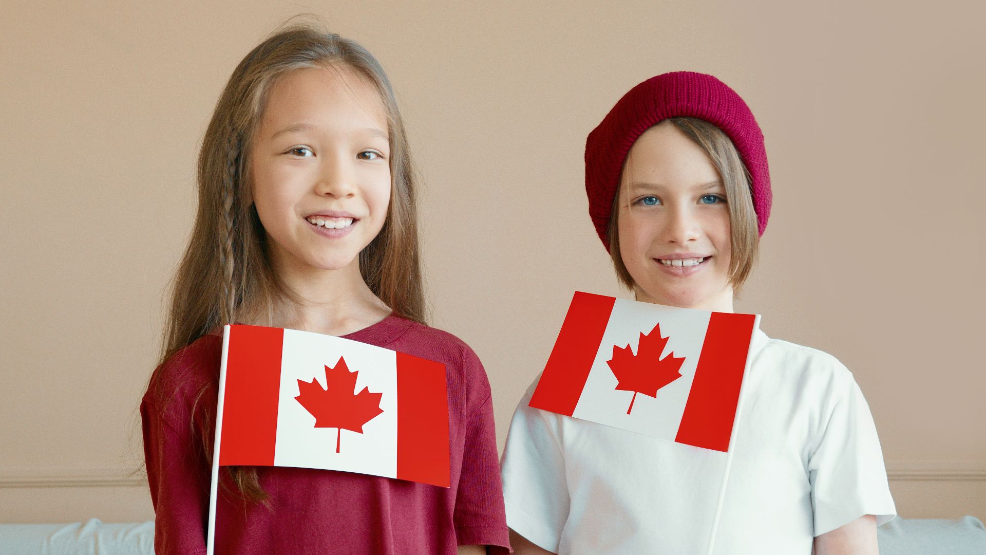 Two smiling children holding Canadian flags indoors, celebrating national pride.