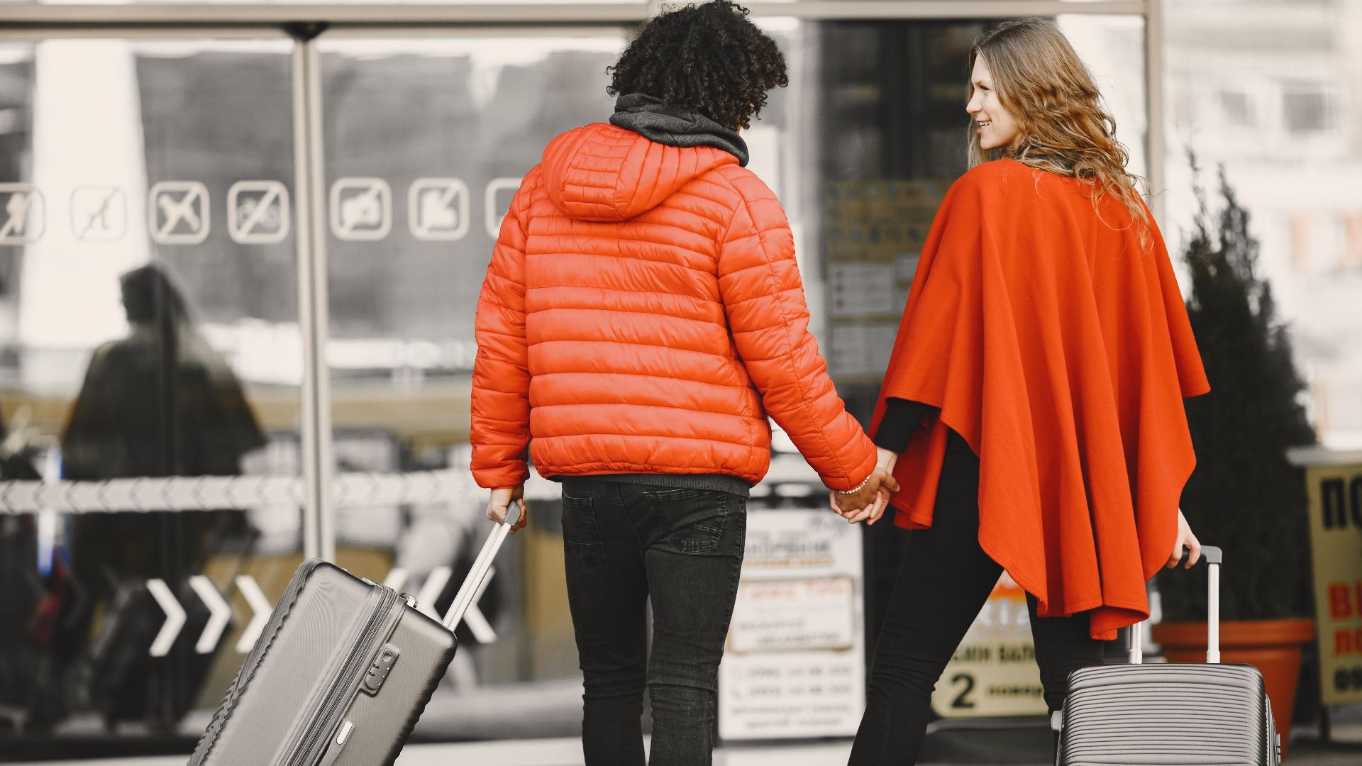 A couple holding hands with luggage, entering an airport for a travel journey.