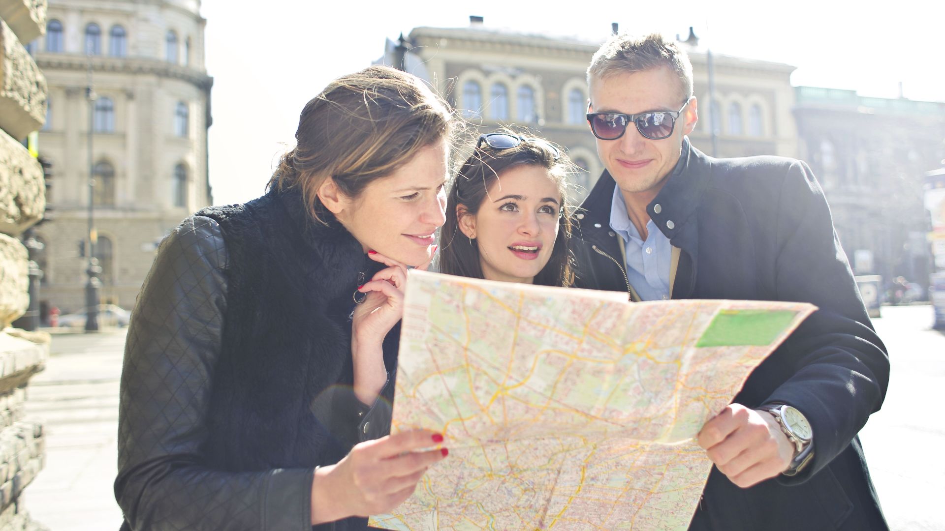 Three tourists exploring a city using a map under bright daylight, enjoying their travel journey.