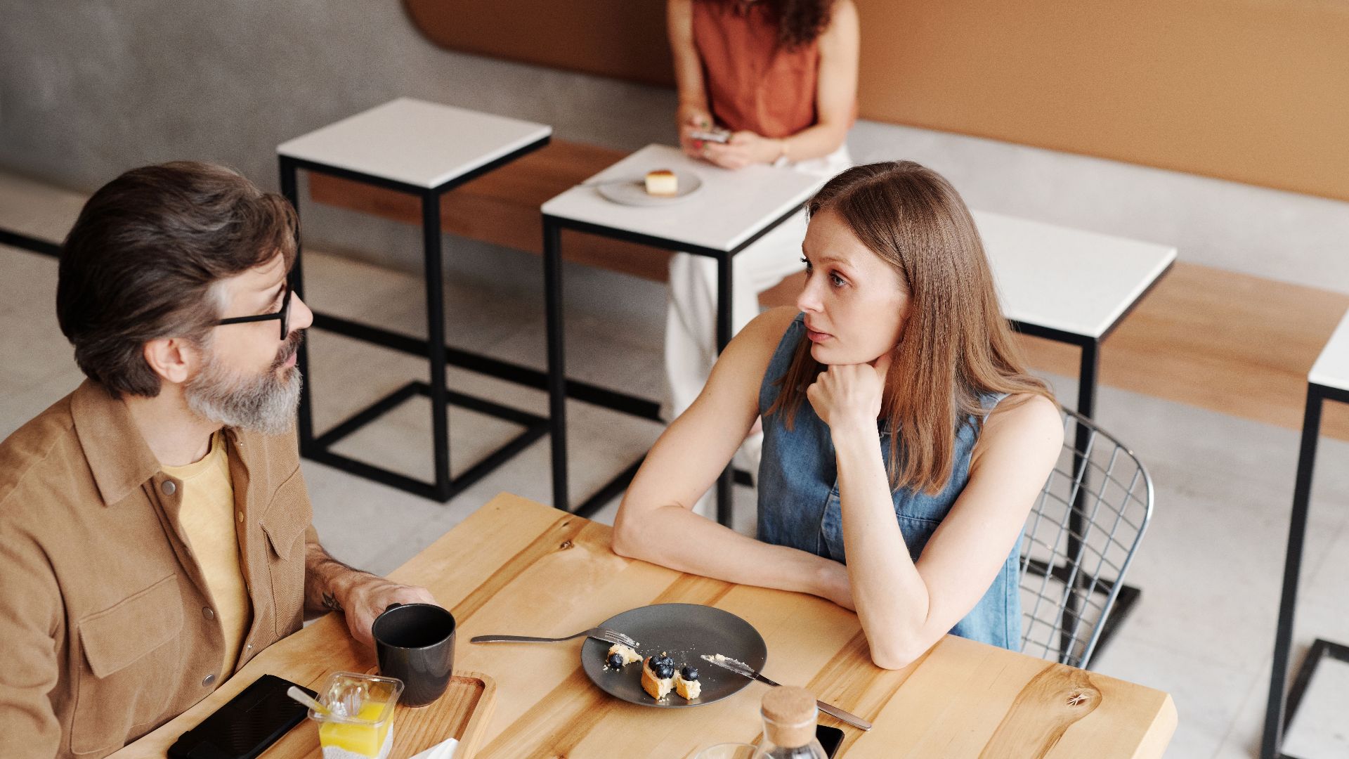 A man and woman engage in conversation over breakfast at a stylish coffee shop.