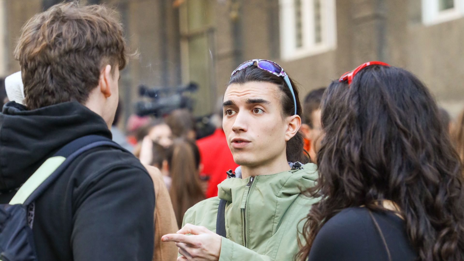 Three young adults talking on a bustling city street, showcasing urban life.