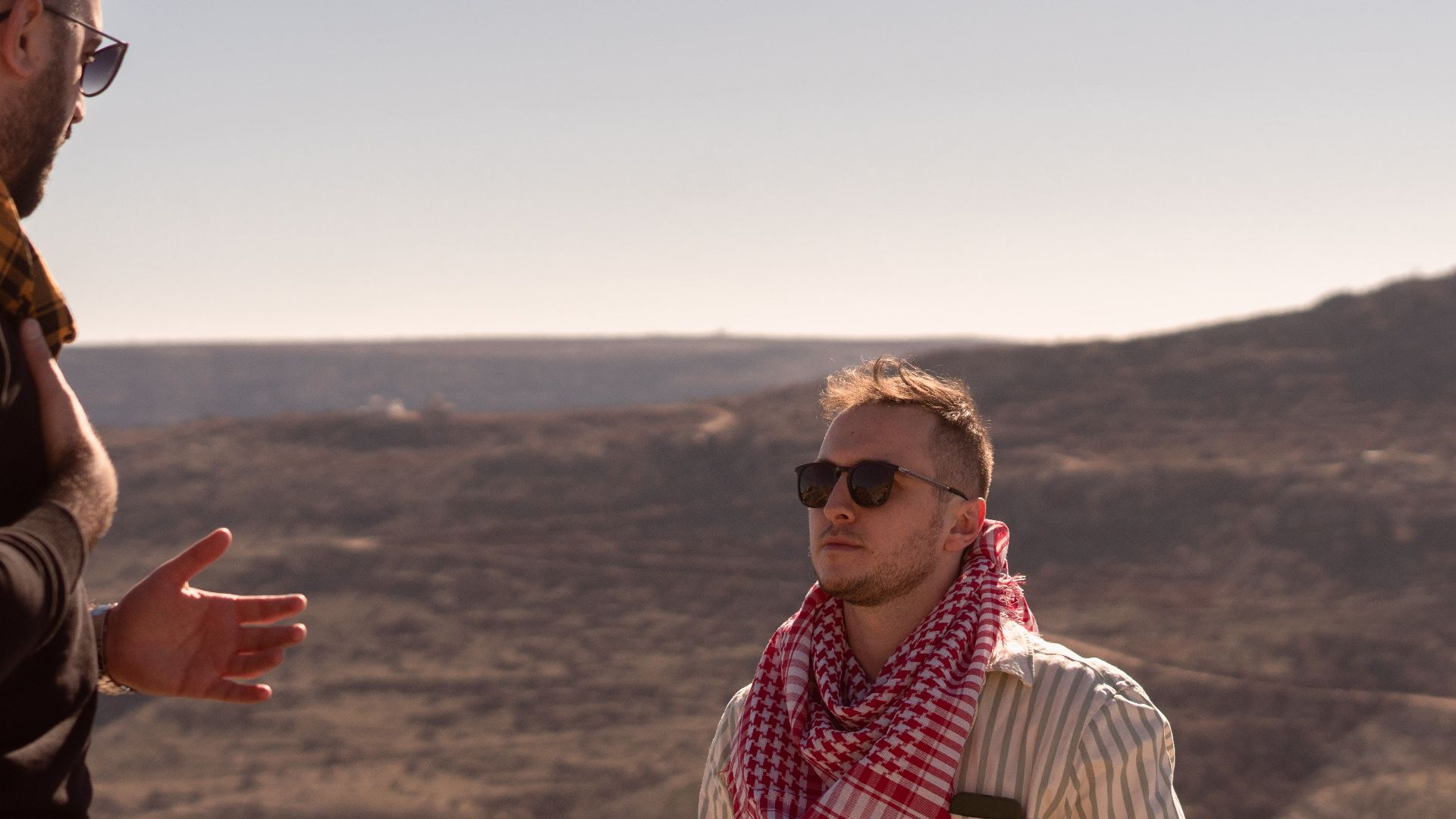 Two men wearing sunglasses and scarves in a sunny desert landscape.