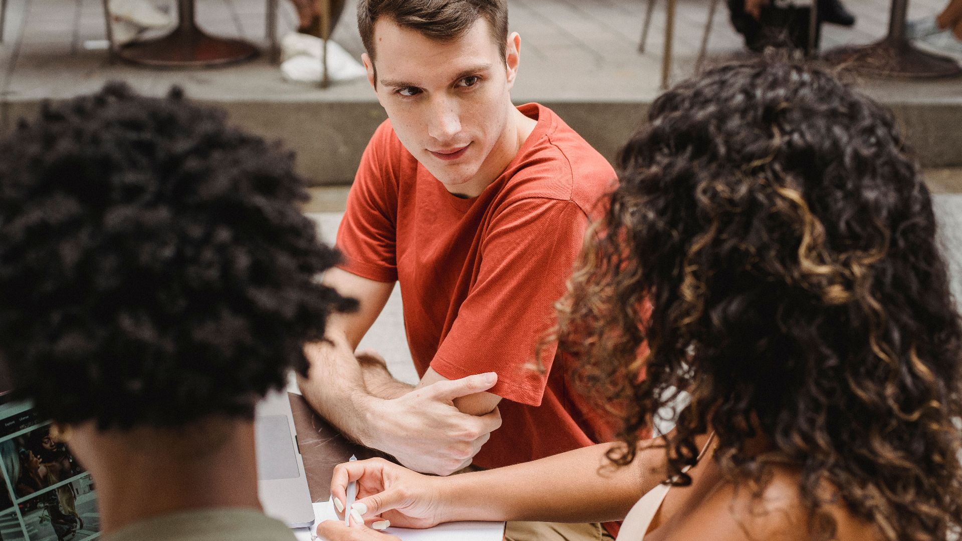 High angle of faceless black man with dreadlocks working on laptop while sitting together with diverse friends discussing homework in modern cafe