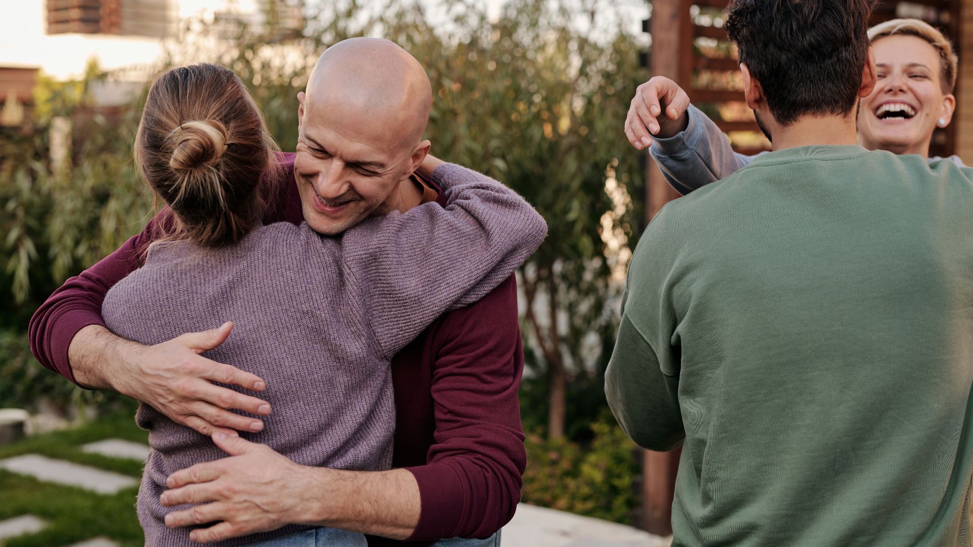 Cheerful friends hugging and smiling while spending time together in suburban yard during weekends