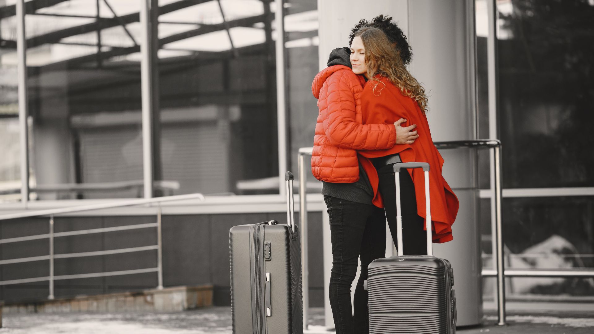 A heartfelt goodbye at the airport with two people hugging and luggage present.