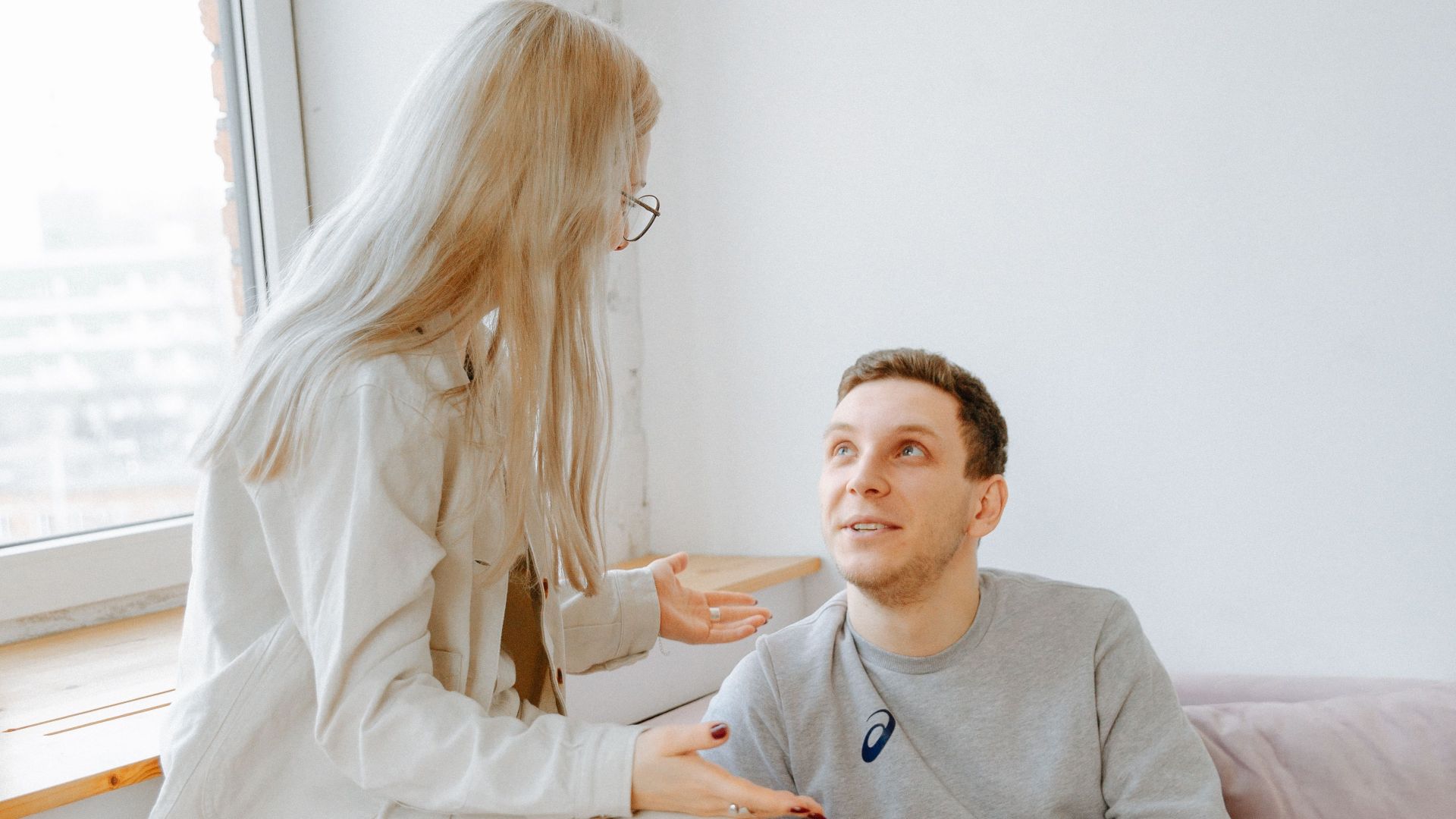 A couple having a conversation on a pink couch in a well-lit modern apartment.