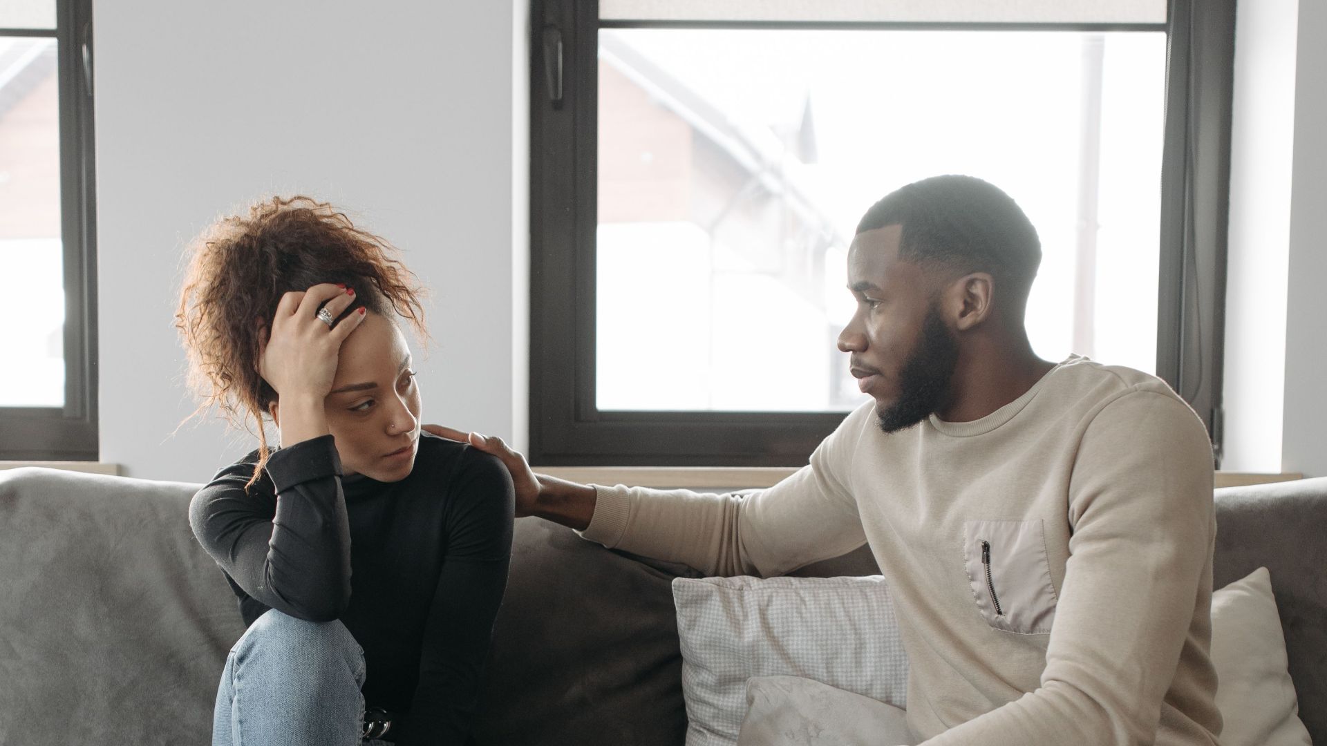 A couple shares a moment on their sofa at home, conveying care and understanding.
