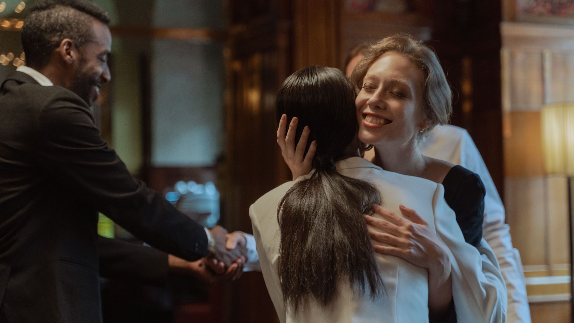 A joyful moment of greeting as two colleagues embrace in a warmly lit office environment.