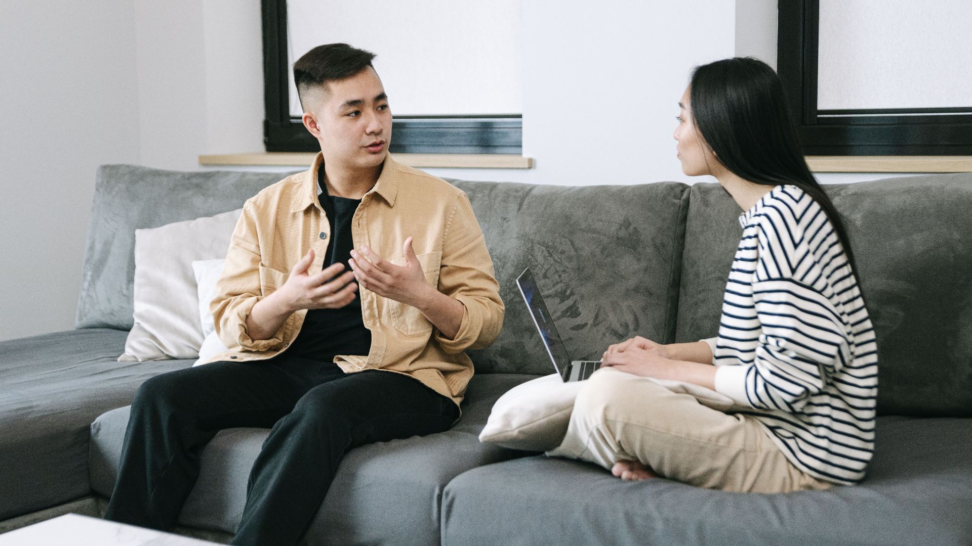 Two young adults engaged in a conversation, sitting on a couch at home.