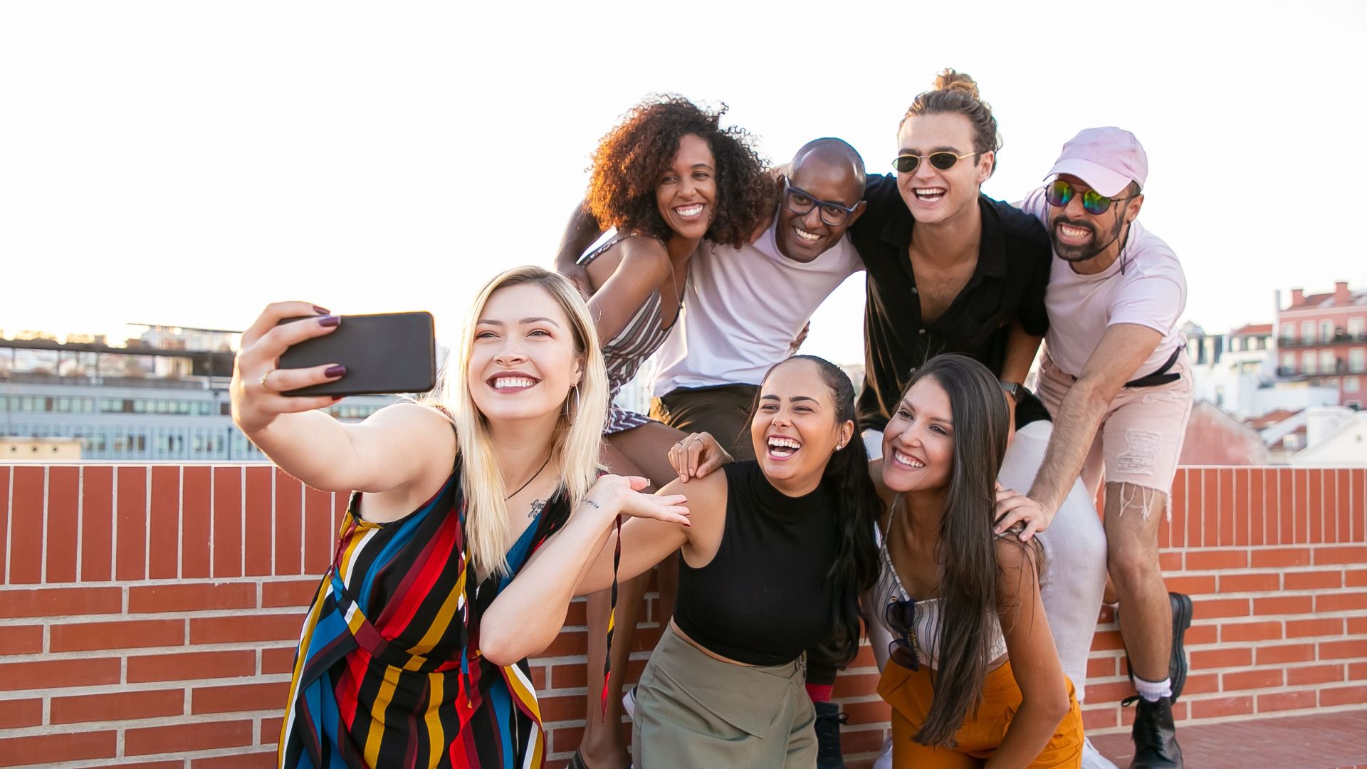 Group of cheerful young male and female multiracial friends laughing and taking selfie on smartphone while spending time together on terrace