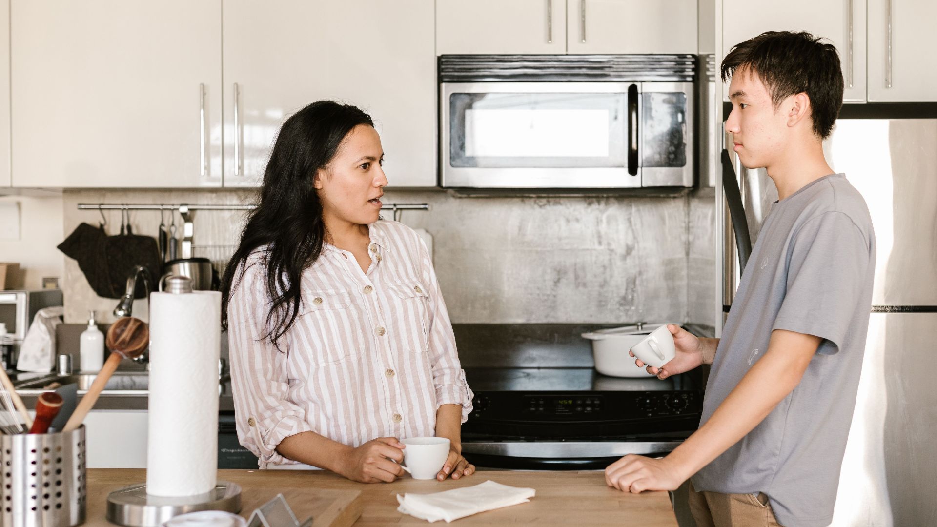 A young man and woman enjoy a casual talk over coffee in a sleek kitchen environment.