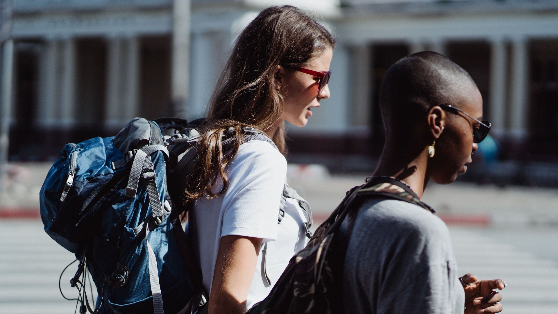 Two diverse women with backpacks exploring a city, enjoying their travel journey.