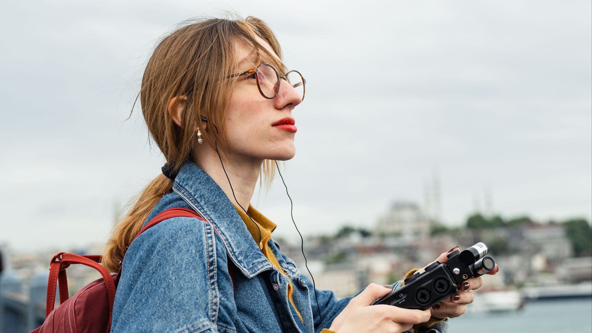 A fashionable woman with a backpack enjoys the view from Galata Bridge in Istanbul, holding a drone controller.