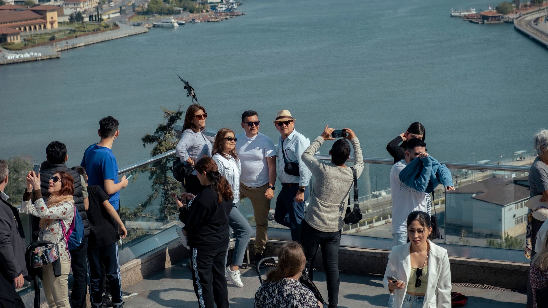 Group of tourists taking photos at a city overlook with a river and bridge in the background.