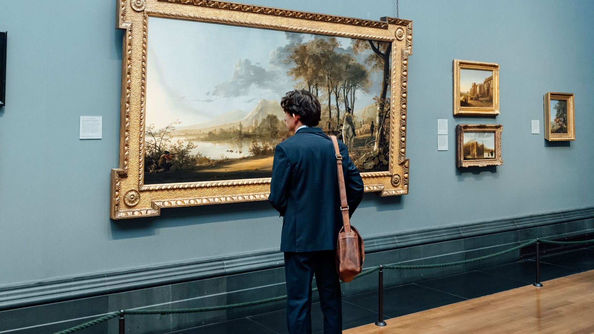 A man observes classic paintings in a London gallery, appreciating art history.