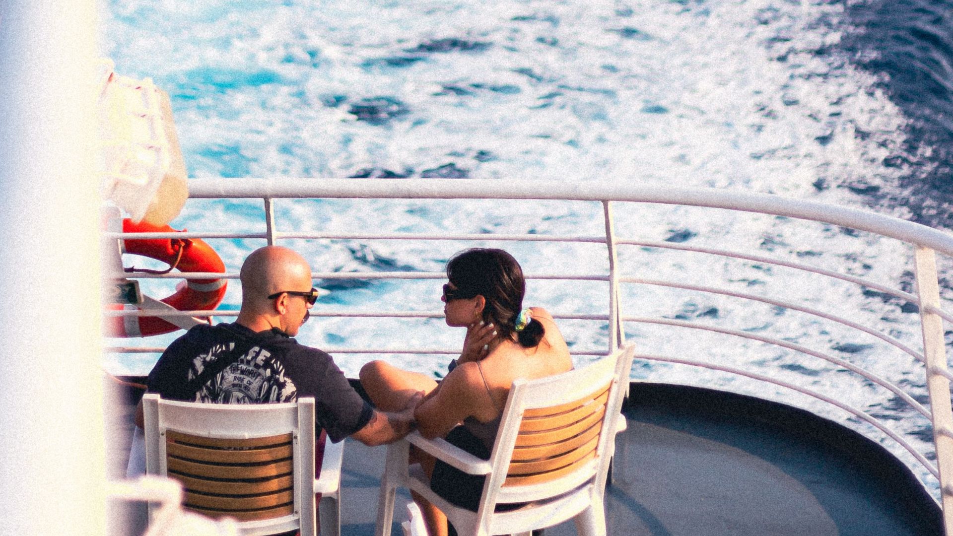 Couple enjoying a calm cruise on a ship, surrounded by ocean waves and clear skies.