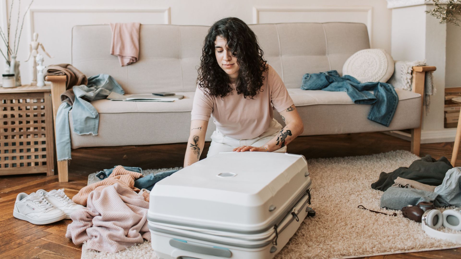 Woman with curly hair packing a suitcase in a stylish living room with a modern, cozy vibe.