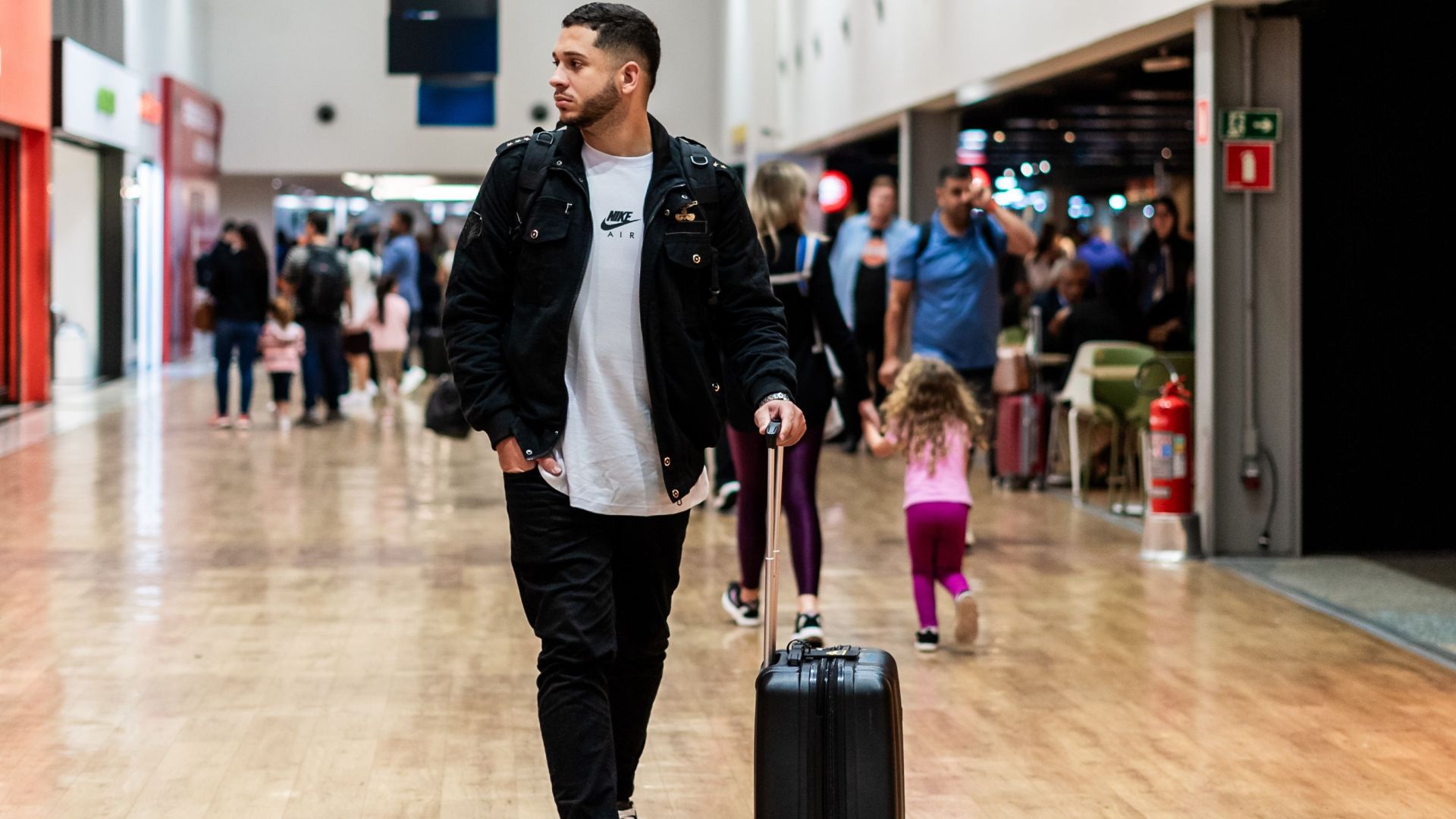 Man walking with luggage in a crowded airport terminal, heading to boarding gates.