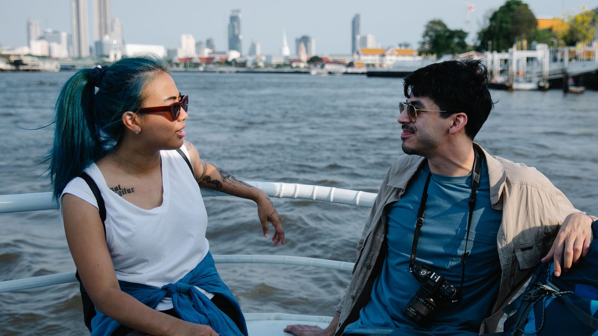 A young couple enjoys leisure time on a boat with a city skyline in the background.