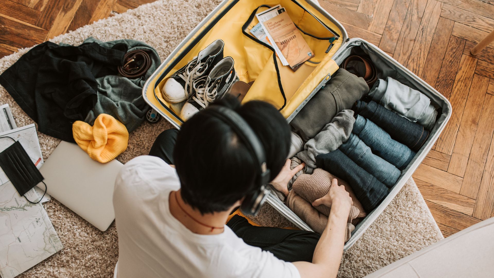 Adult packing clothes in a suitcase while listening to music at home. Overhead view on rug.