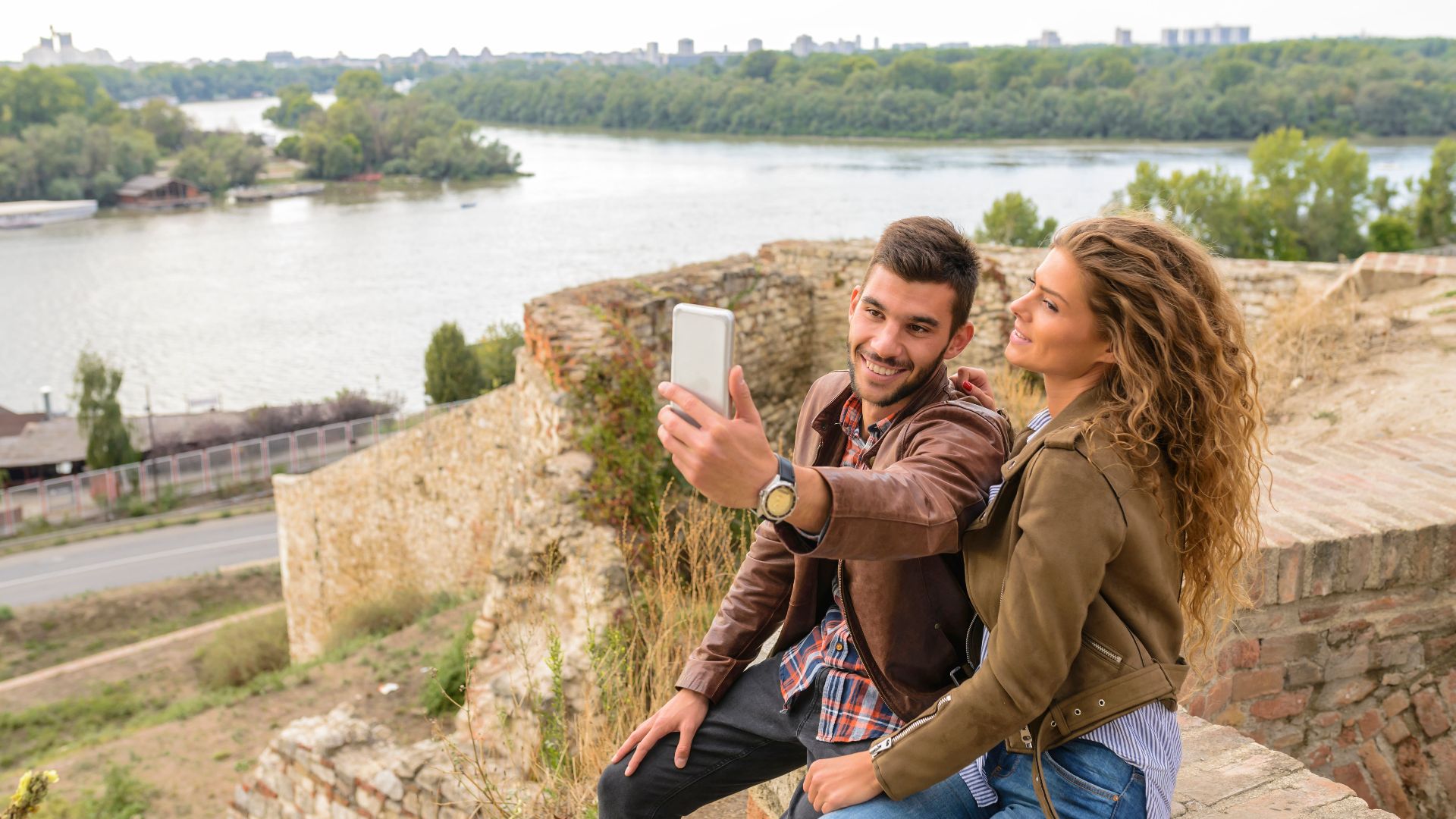 Happy couple takes a selfie at a scenic riverside location, enjoying their time outdoors.