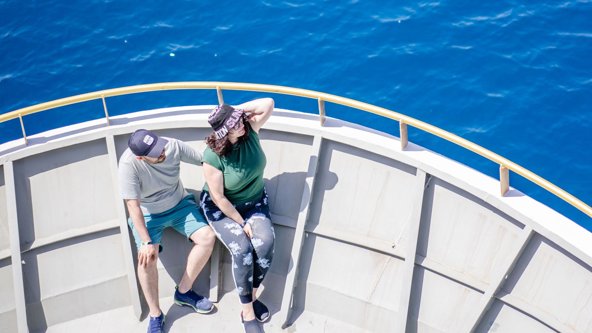 A couple sits on a yacht deck enjoying a sunny day over the ocean. Top view captures relaxation.