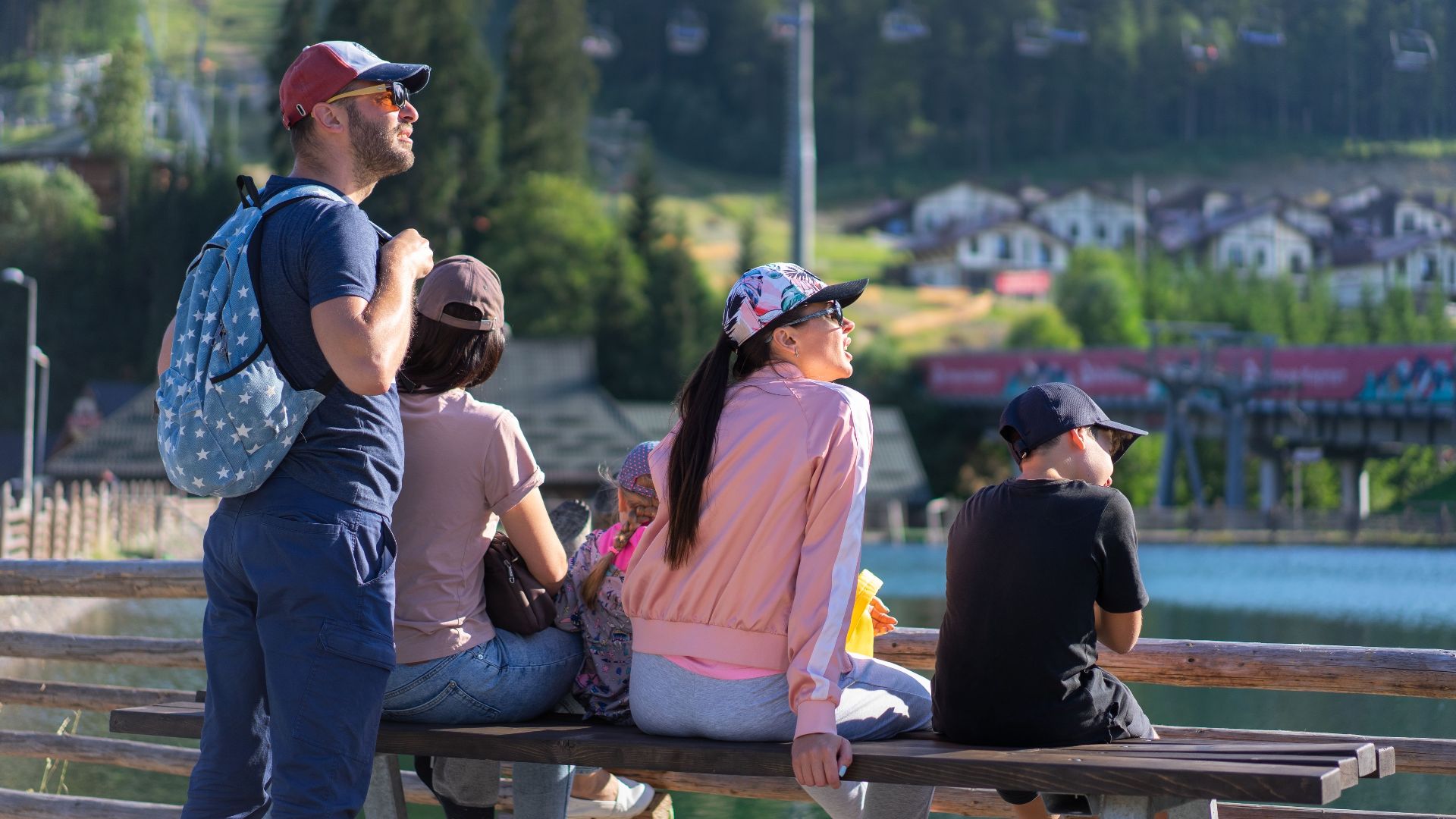 A family enjoys a sunny day sitting on a bench in Bukovel, Ukraine, with scenic mountain views.