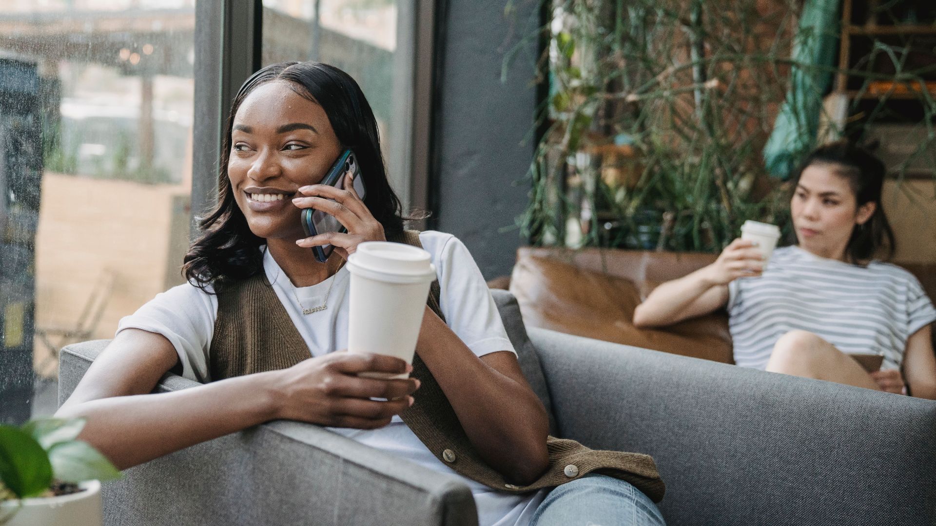 Two women enjoying coffee and a phone call in a cozy, urban café setting.