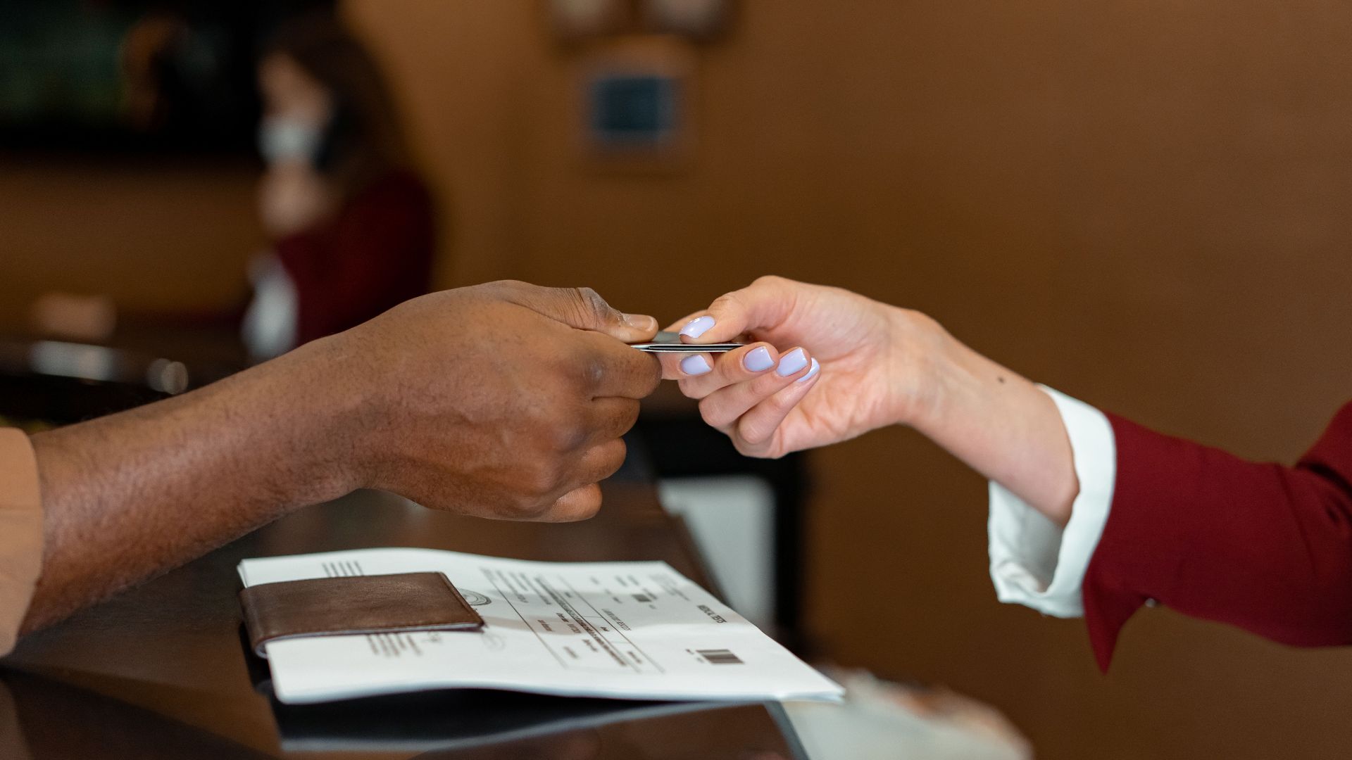 Close-up of a hotel receptionist receiving a credit card from a guest, highlighting a transaction at check-in.