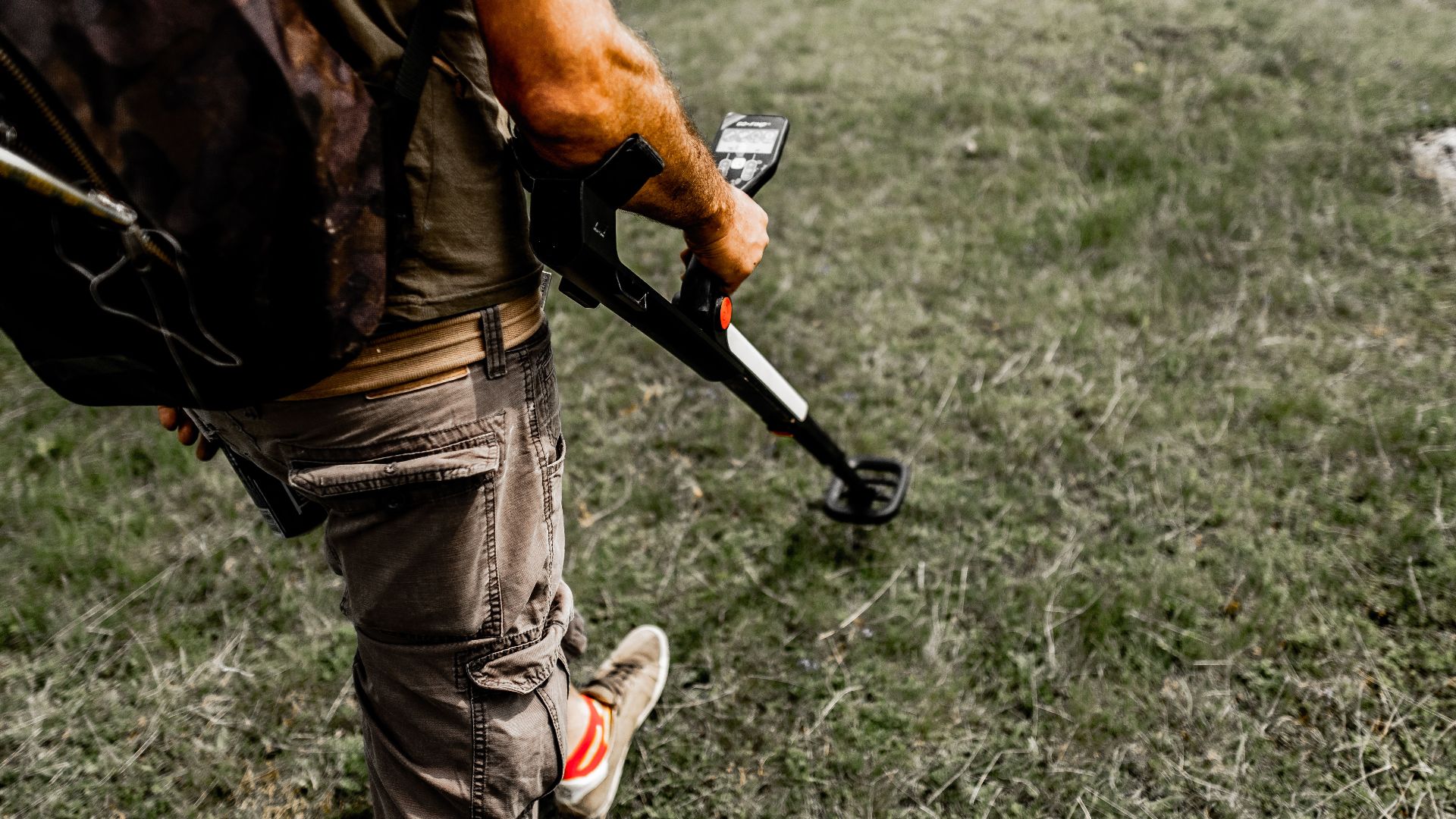 Person using a metal detector on a grassy field wearing casual attire.