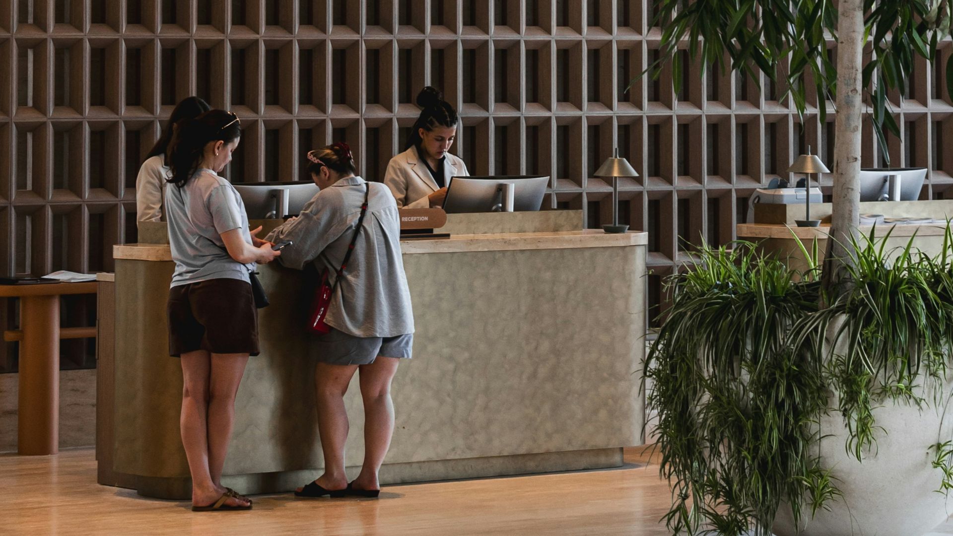 Modern hotel lobby reception with guests, tree, and wall art.
