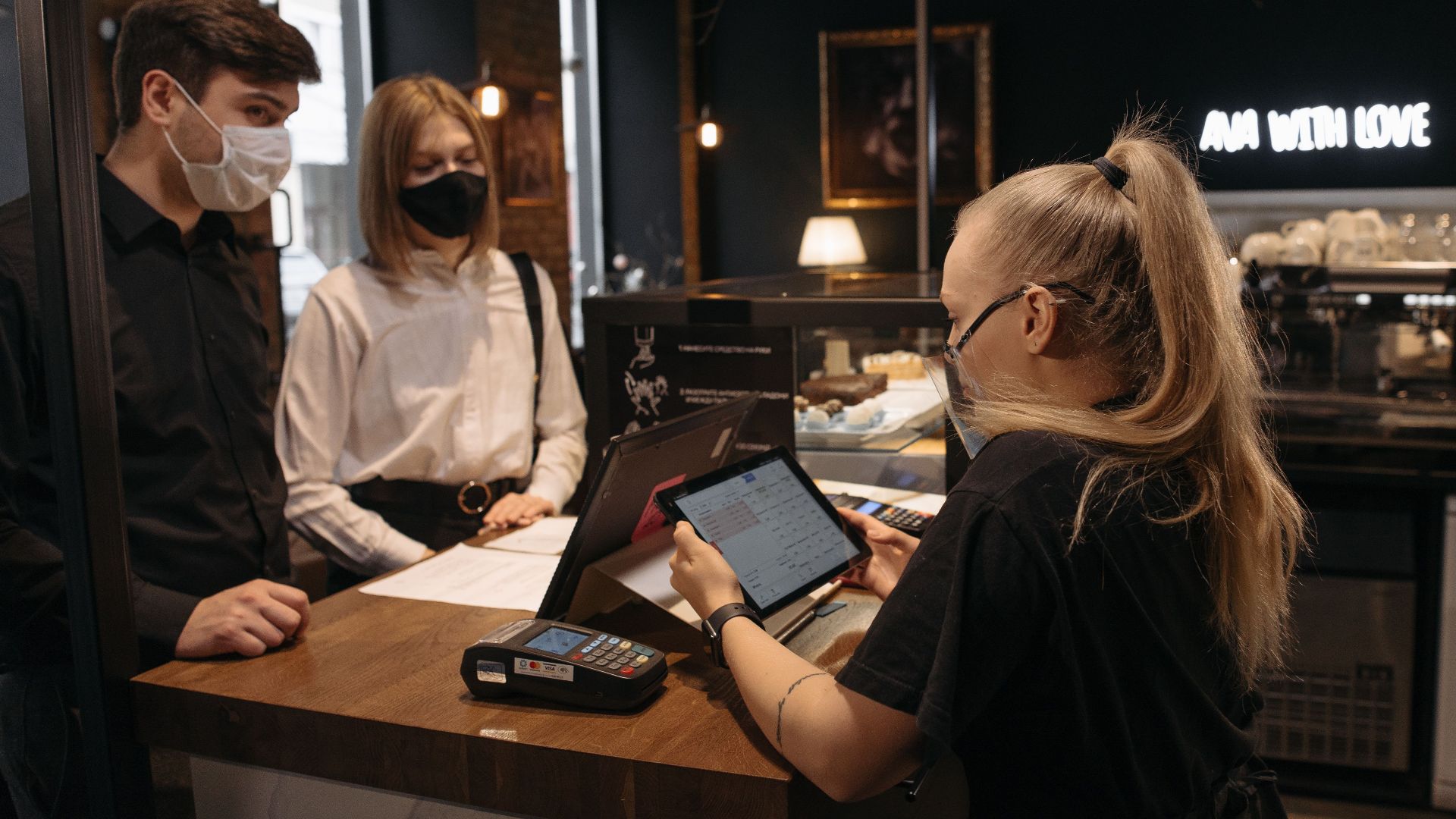 Customers place an order at a café counter with a barista using a tablet for payment.