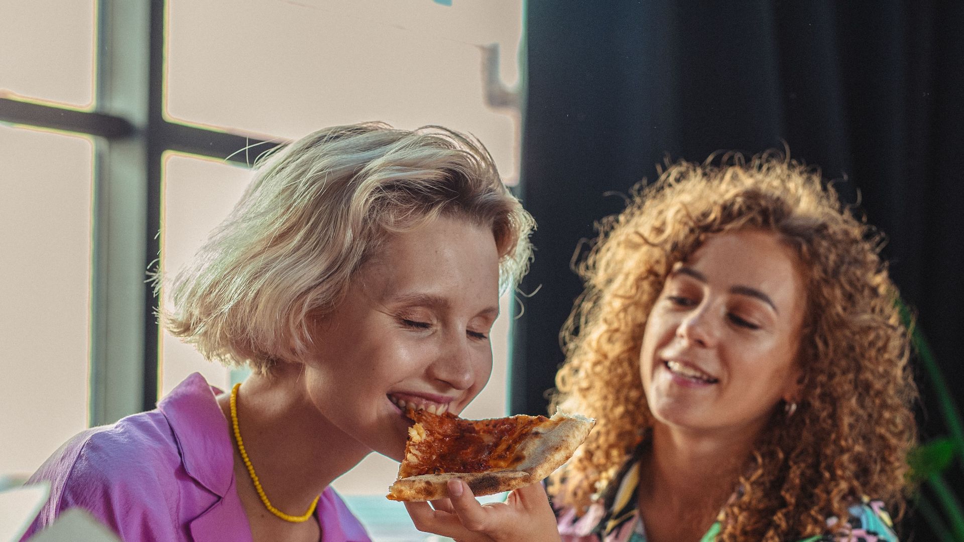 Two women enjoying pizza together in a cozy home setting, capturing love and warmth.