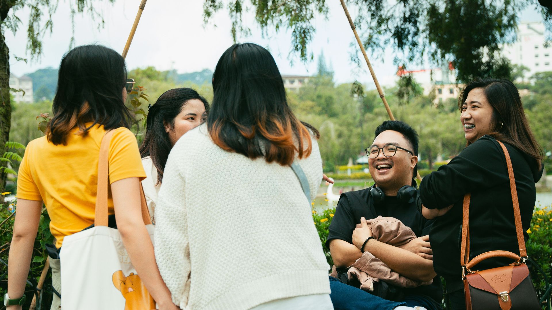 A group of Asian friends enjoying a relaxed time in a park during the day, smiling and talking.