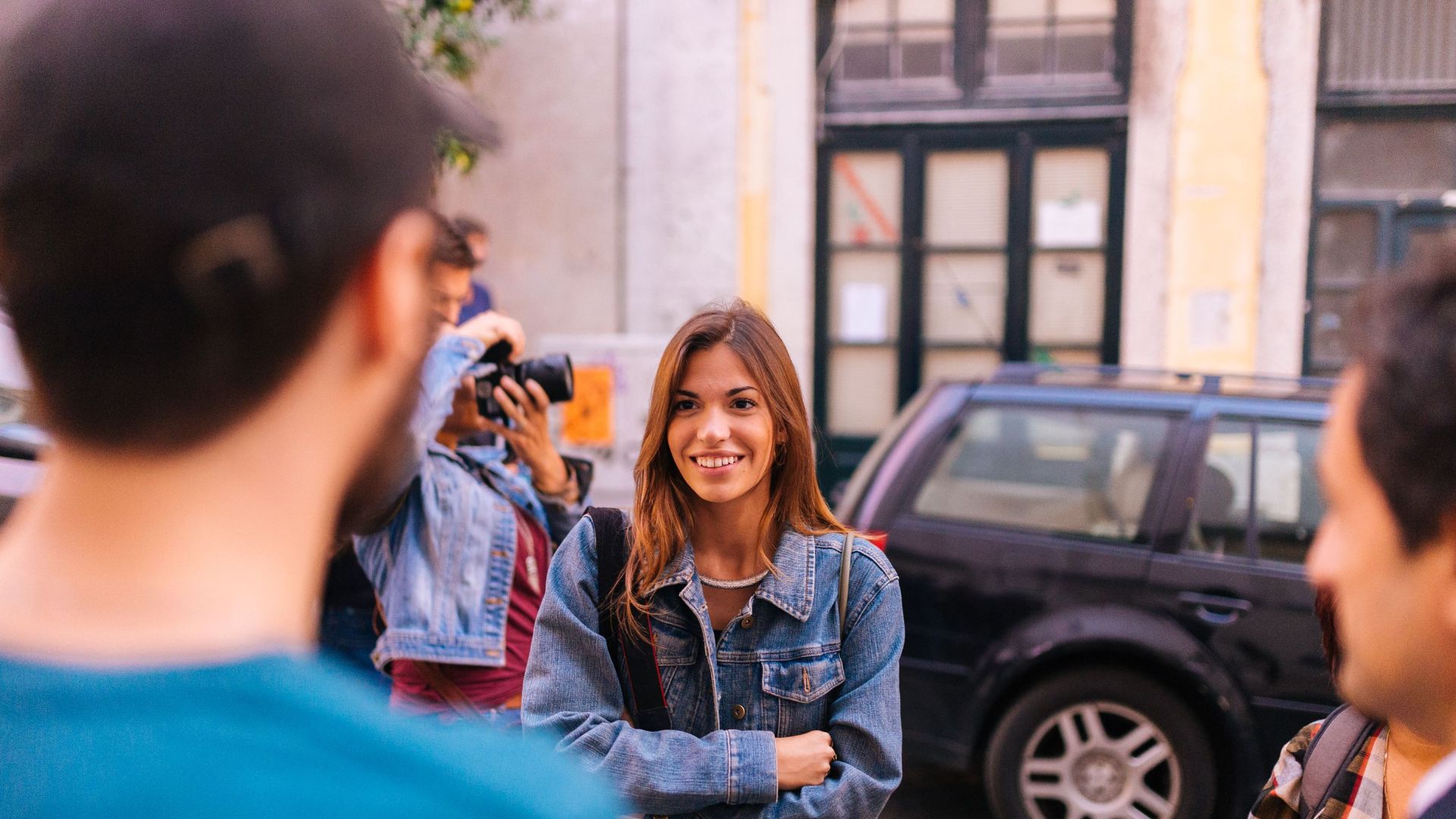 A group of friends smiling and interacting on a city street during the day.