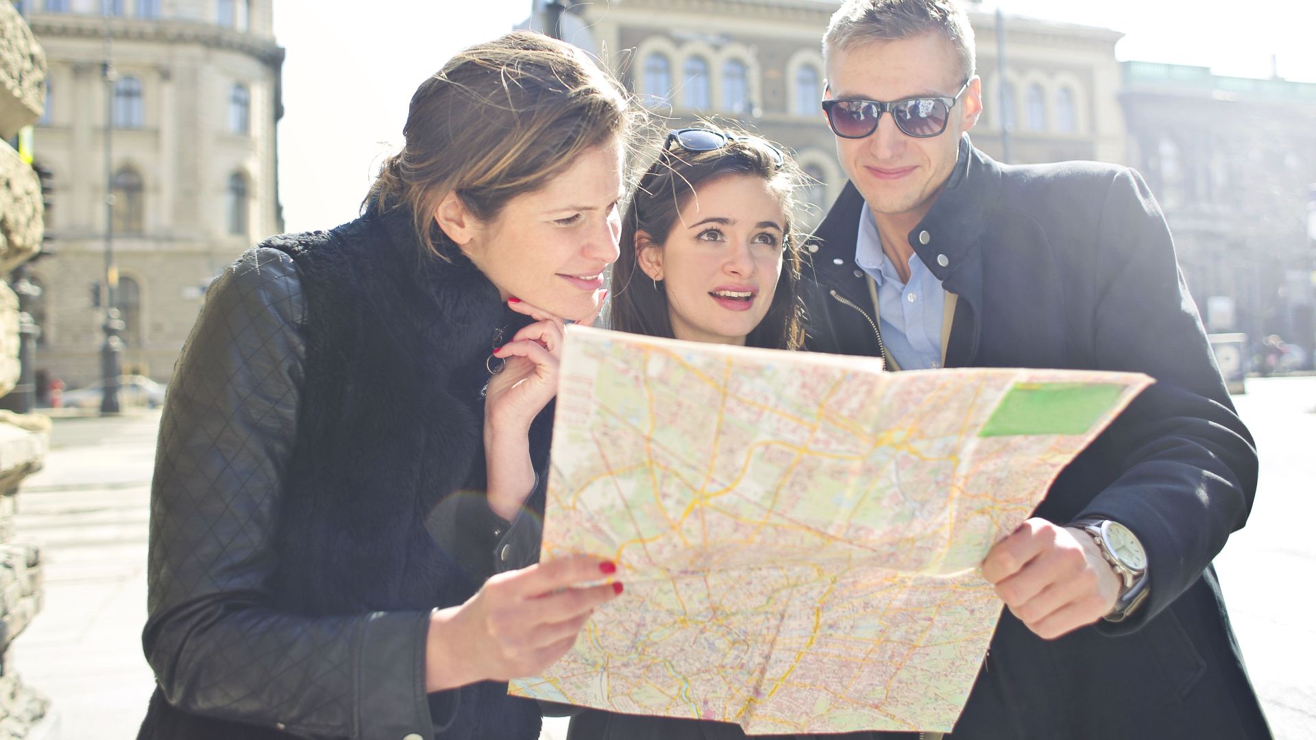 Three tourists exploring a city using a map under bright daylight, enjoying their travel journey.