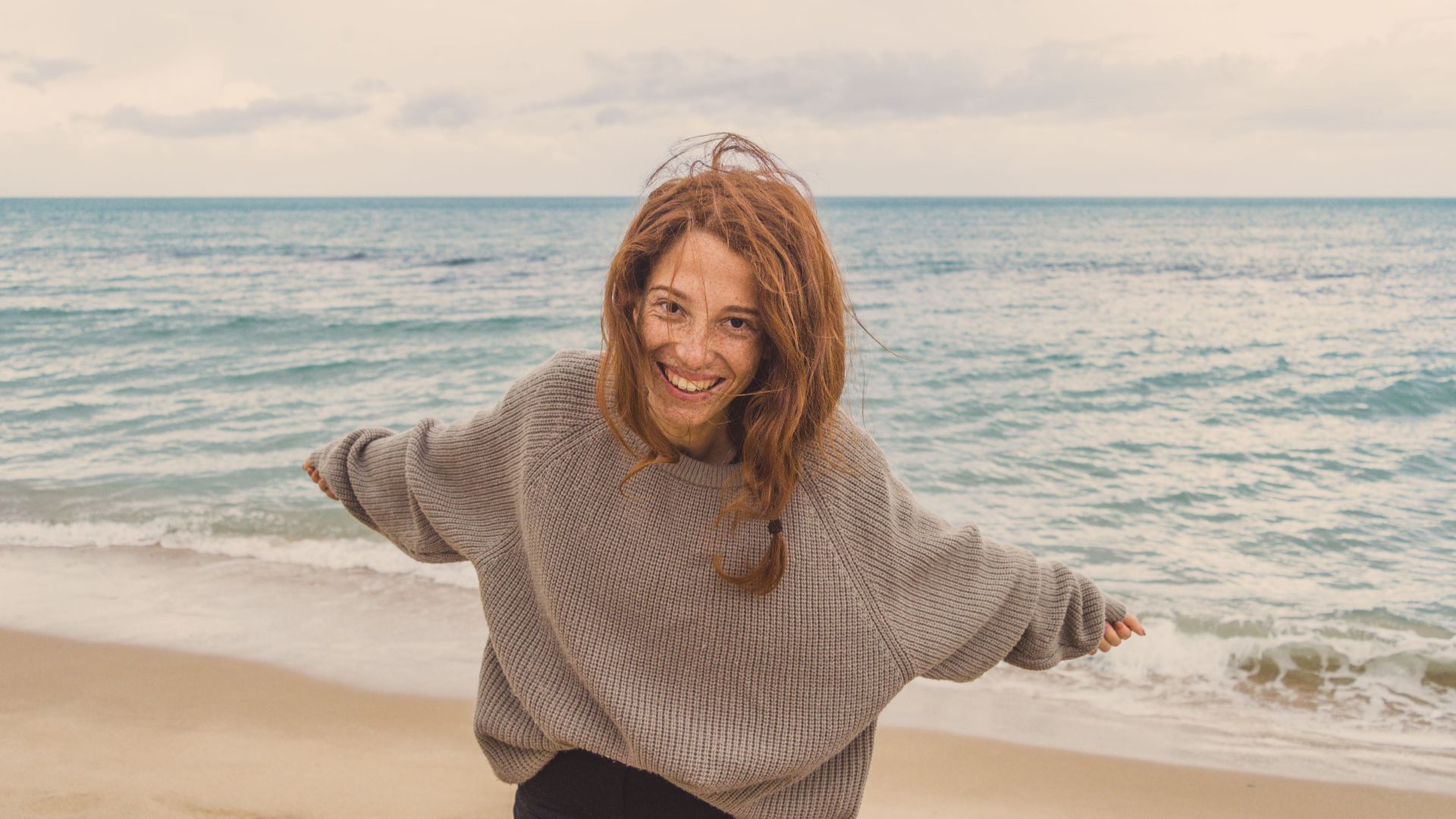 Happy woman with open arms on a serene beach embracing the coastal breeze.