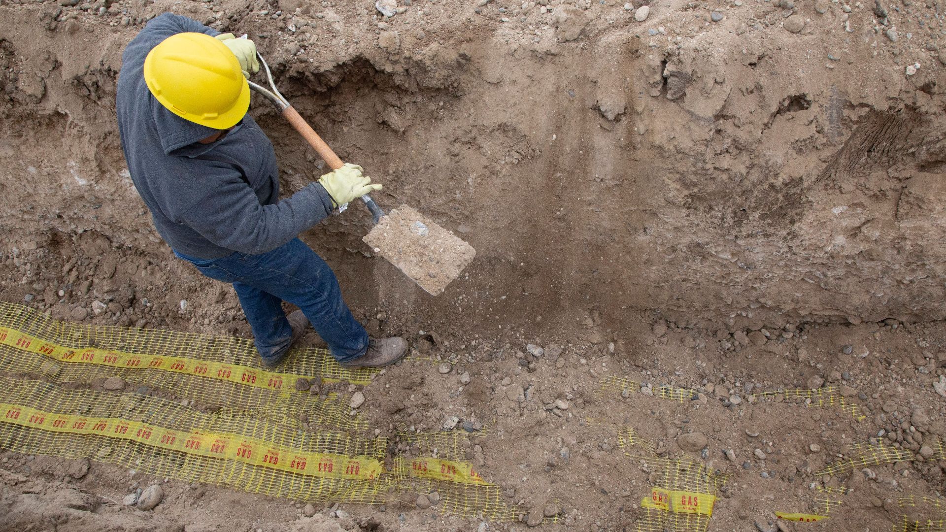 Overhead view of a construction worker digging a trench using a shovel at a site.