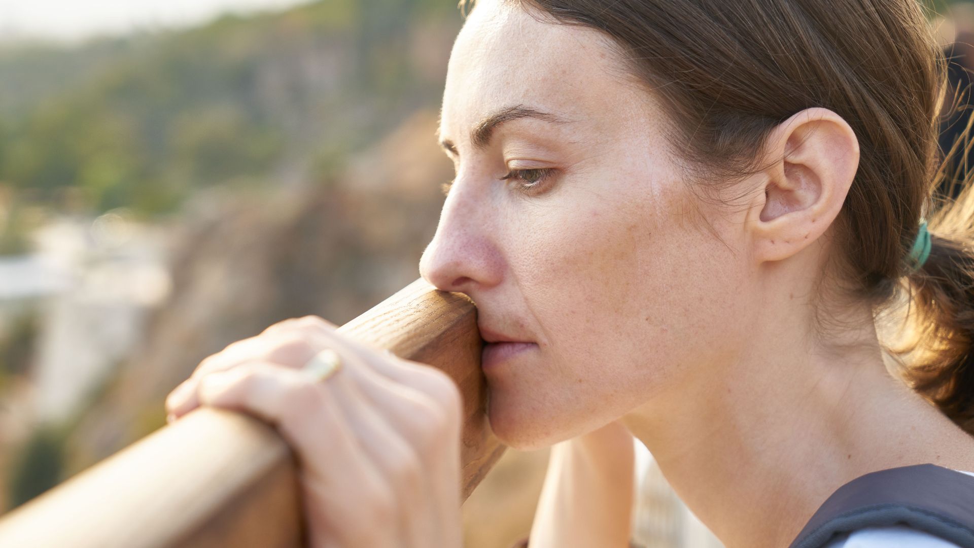 A thoughtful woman leans on a railing, lost in deep contemplation outdoors.