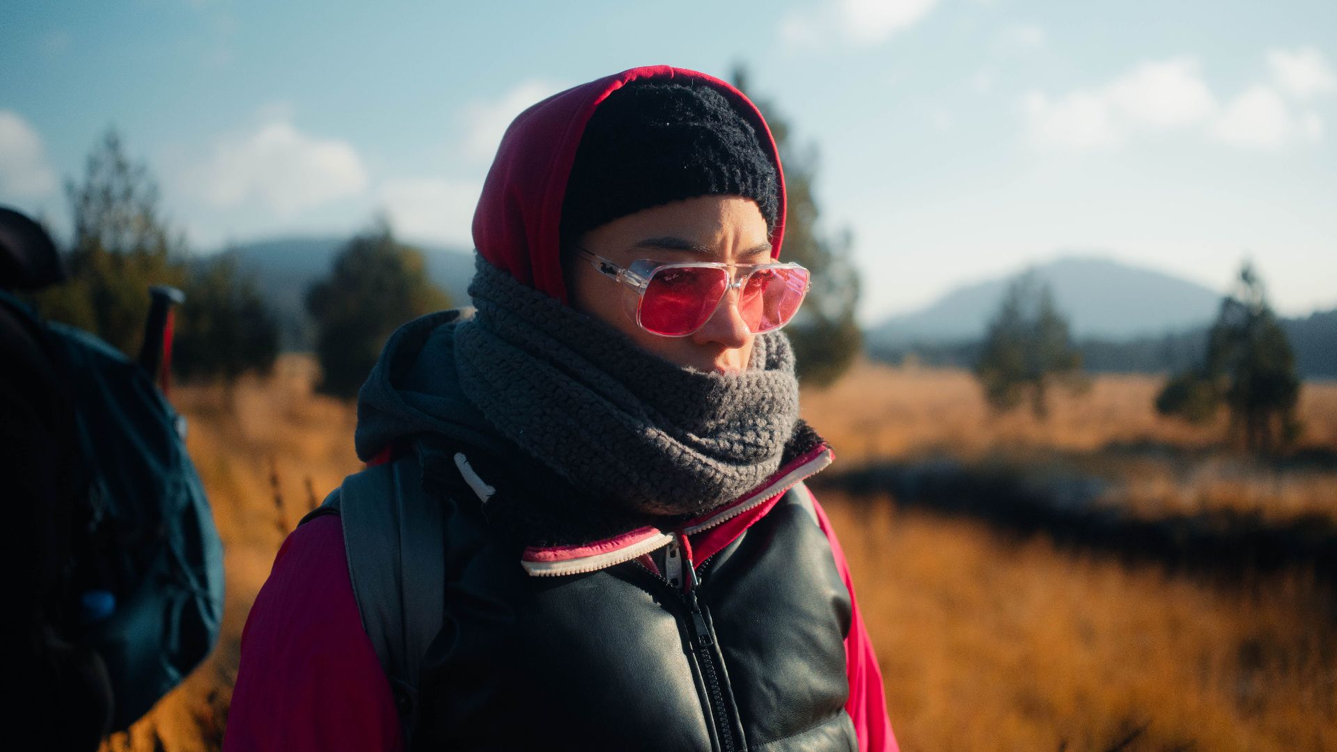 A person warmly dressed with pink sunglasses enjoying an autumn hike.