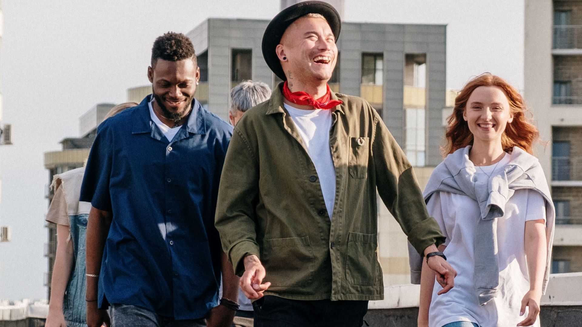 Diverse group of friends laughing and walking on an urban rooftop, enjoying a sunny day.