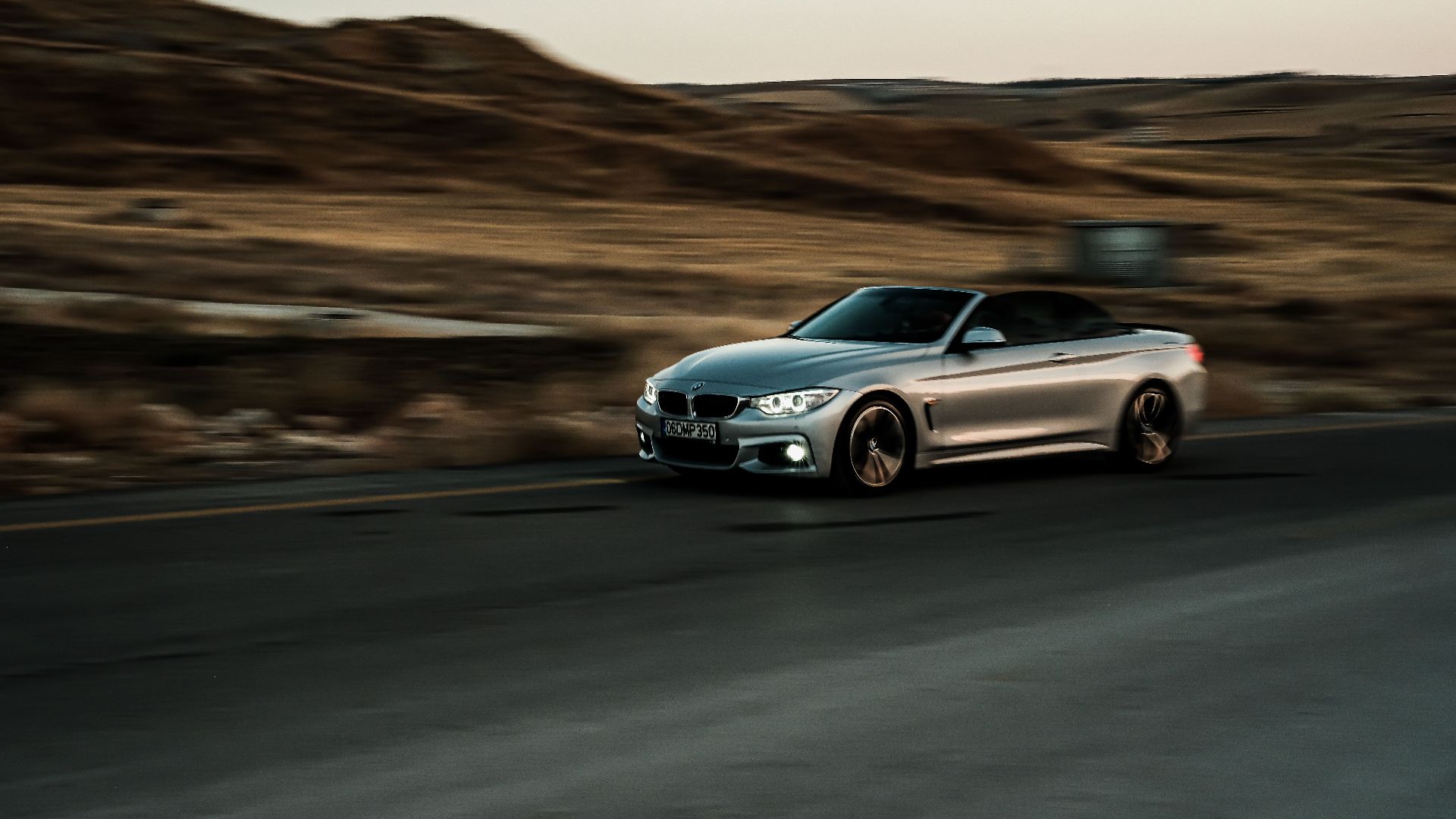A sleek silver convertible car captures motion on a highway, showcasing luxury and speed.