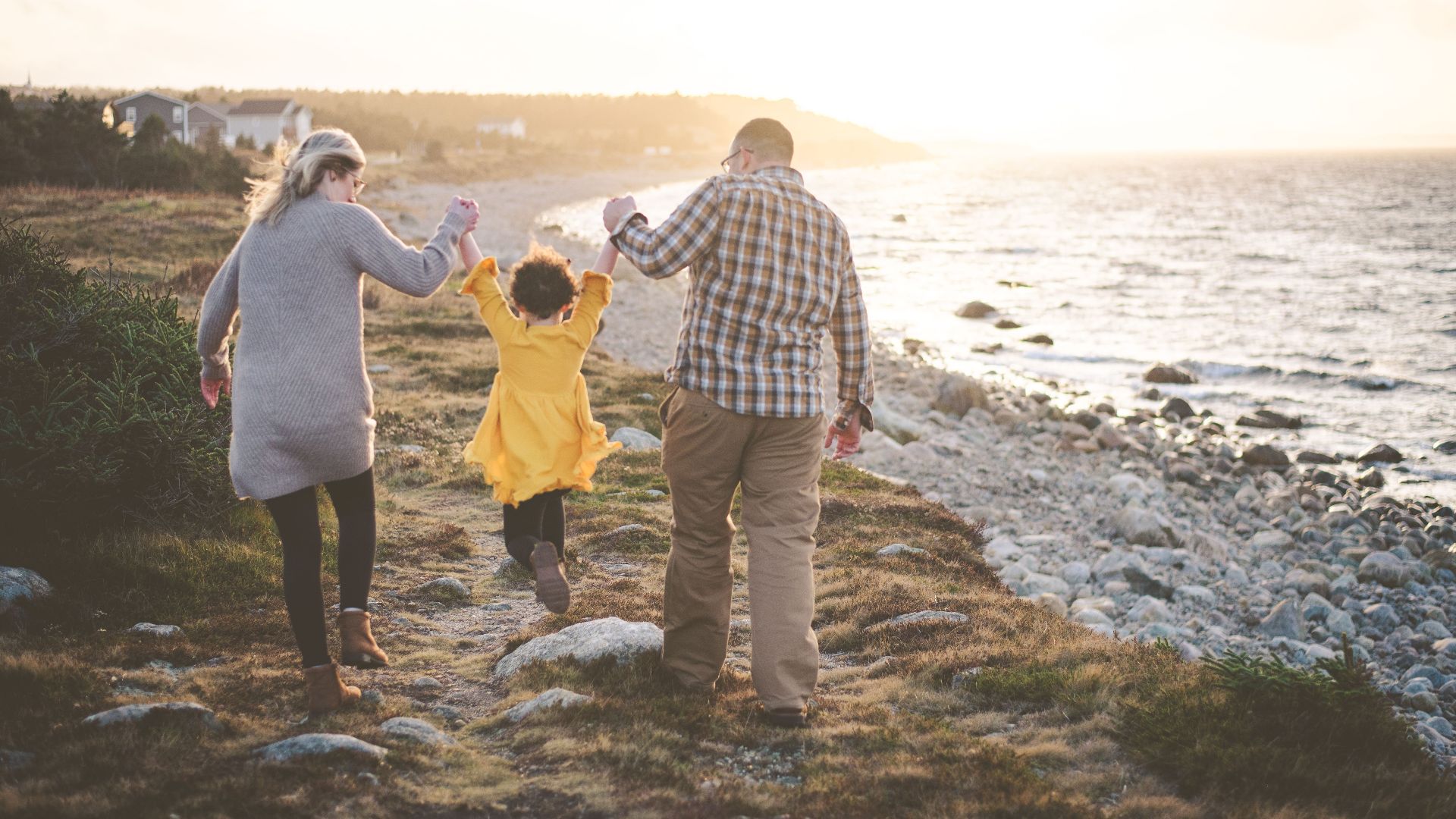 Parents and child enjoy a seaside walk at sunset, holding hands.