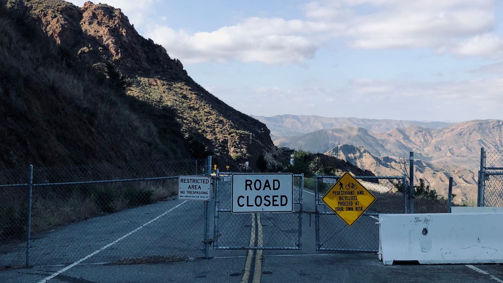 A metal gate blocks a mountain road with scenic views in the background.
