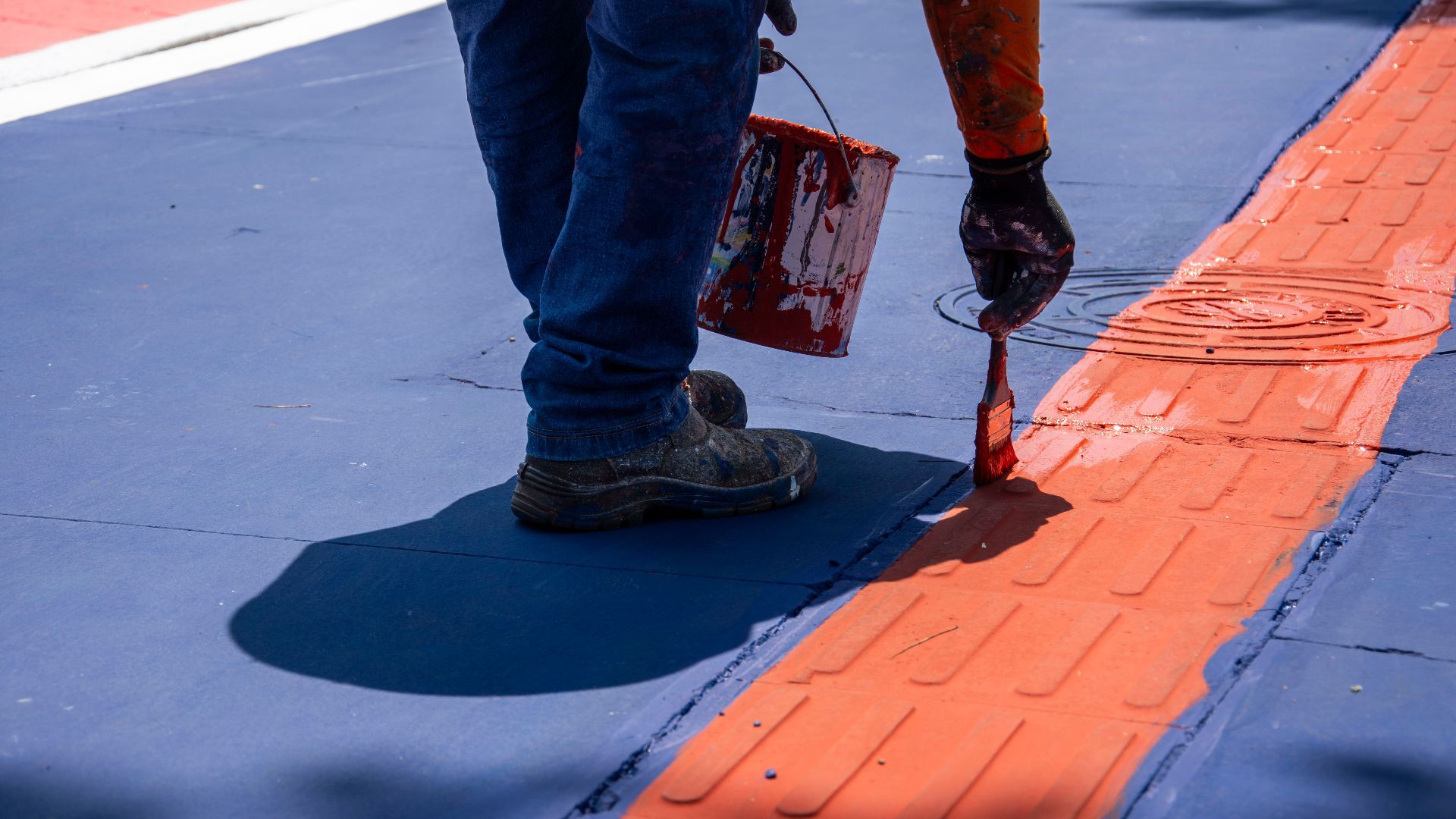 A person paints a red line on a city street, adding vibrant color to the environment.