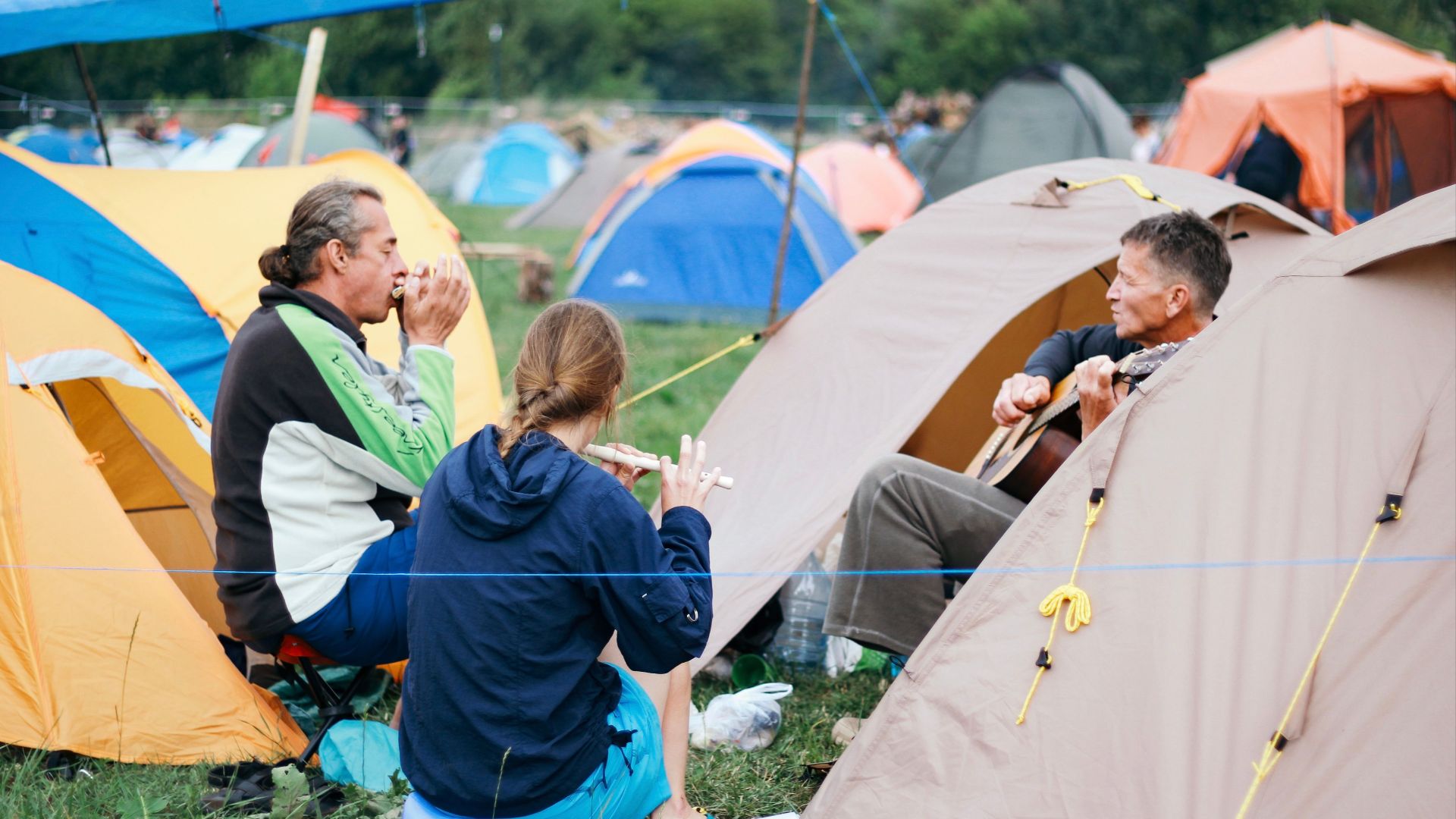 A group of campers playing music and bonding at a campsite outdoors.