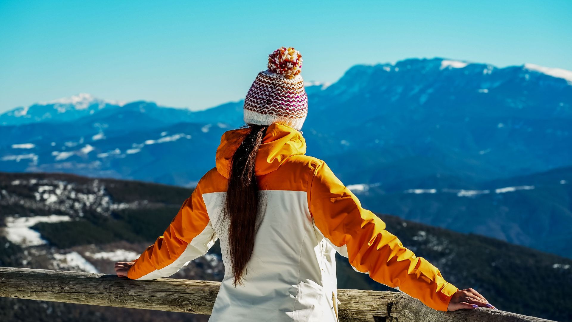 Woman in warm clothing admires breathtaking mountain view on a sunny winter day.