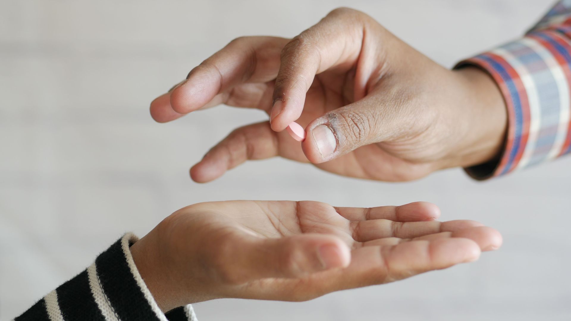 Close-up of hands exchanging a single pill, symbolizing medication sharing.