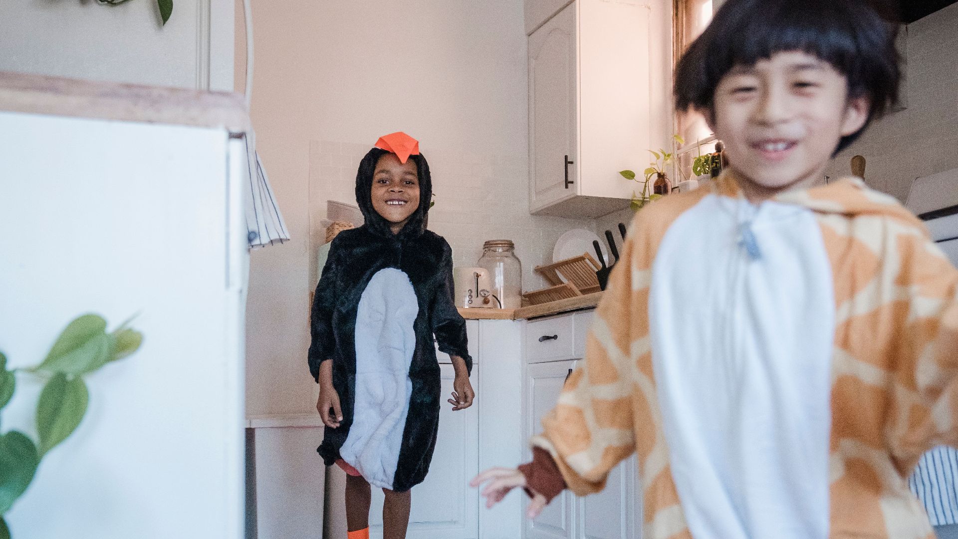 Two children in animal onesies playing in a kitchen, enjoying a fun and joyful moment.