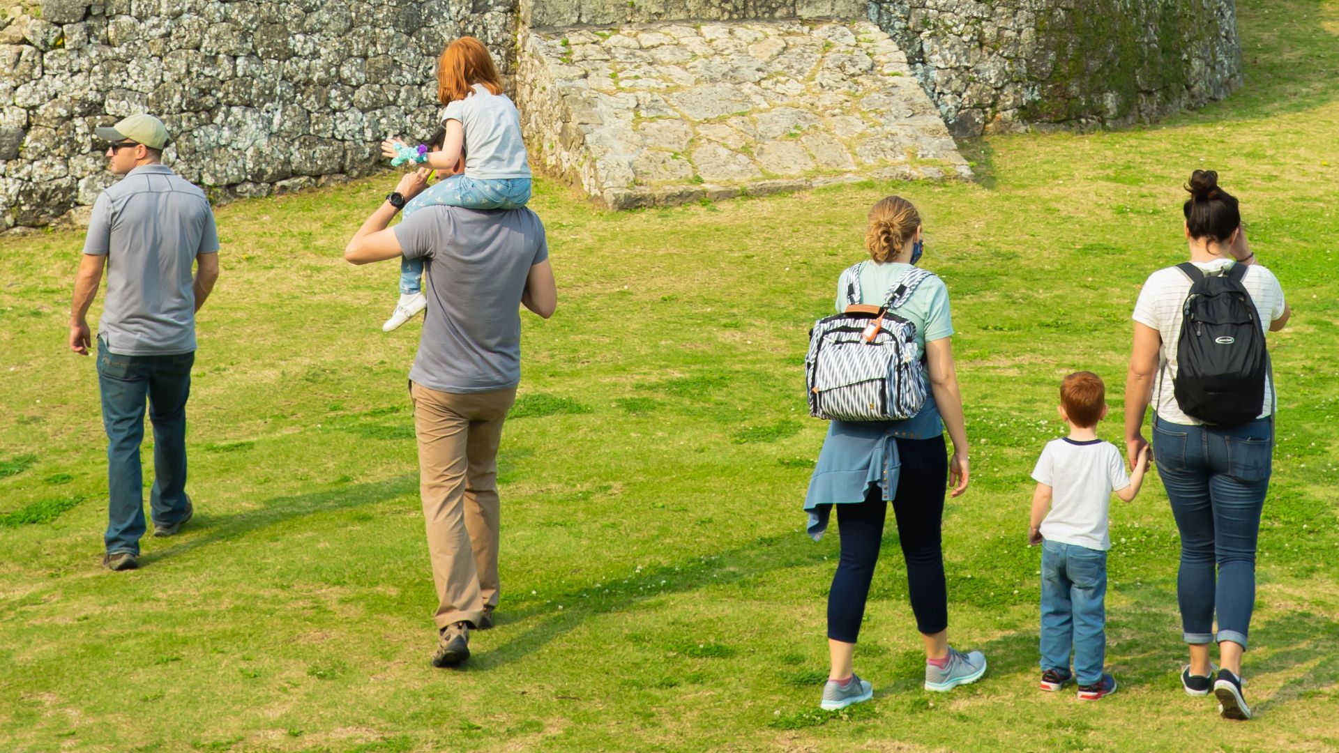 Tourists walking near old stone structure offering panoramic view of city under cloudy sky in daytime